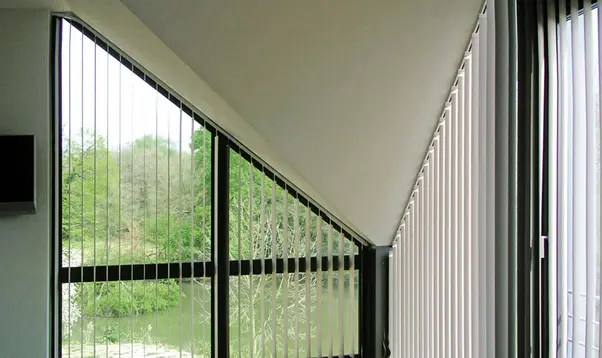 Vertikale Stoffbahnen an einem schrägen Fenster mit Blick ins Grüne